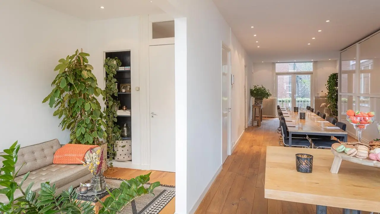 Moderne en ruim ingerichte kantoorruimte aan de Van Baerlestraat met houten vloer, lange vergadertafel en veel groen.